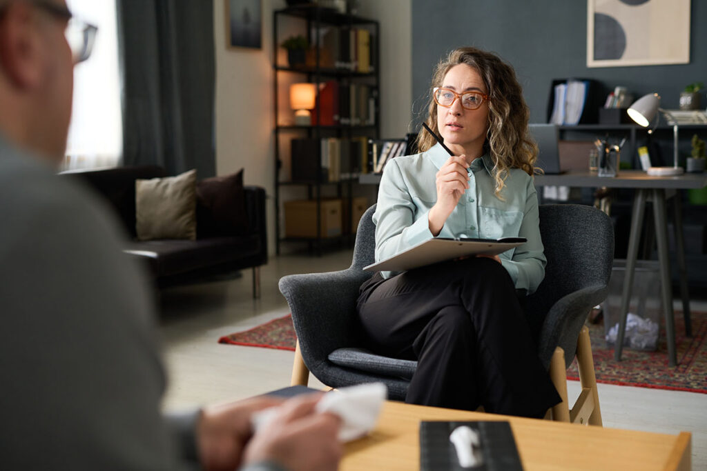 therapist seated behind a desk speaks to a professionally dressed concerned woman who asks, "Can I make someone go to rehab?"