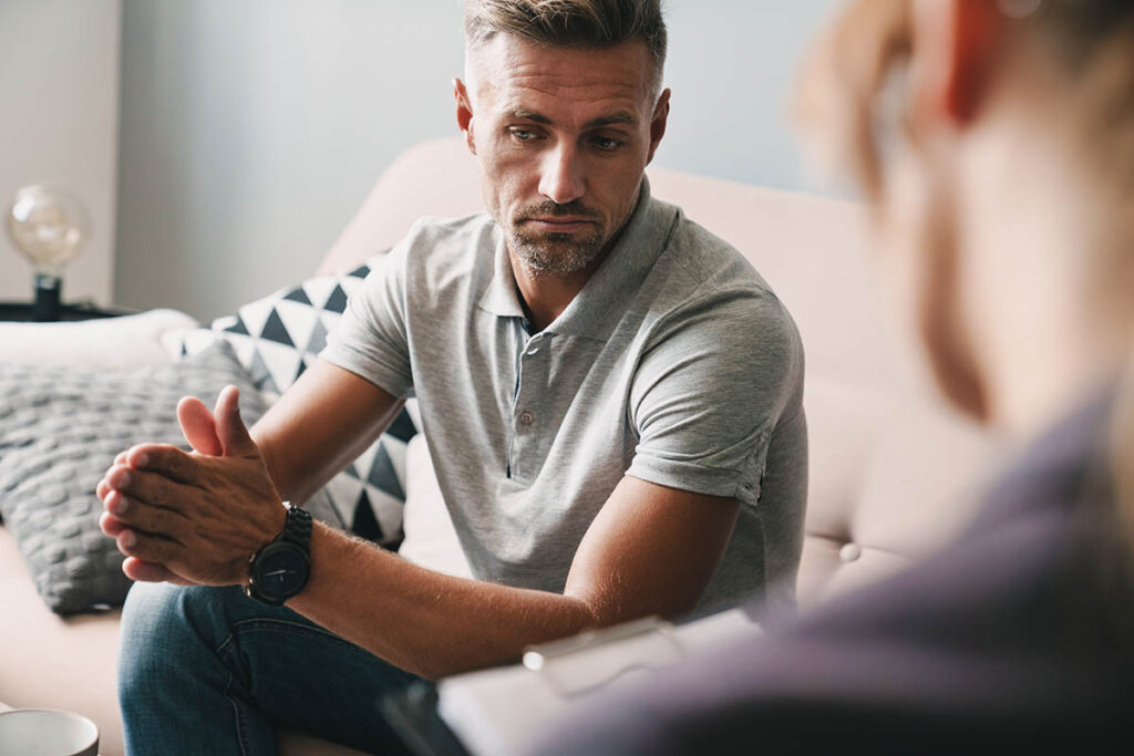 concerned middle-aged man seated in professional setting asking behavioral health professional how does prescription drug addiction start and what are the early warning signs for prevention.