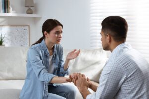 Woman sitting on a couch talks emotionally while a man holds her hands, listening and offering comfort.